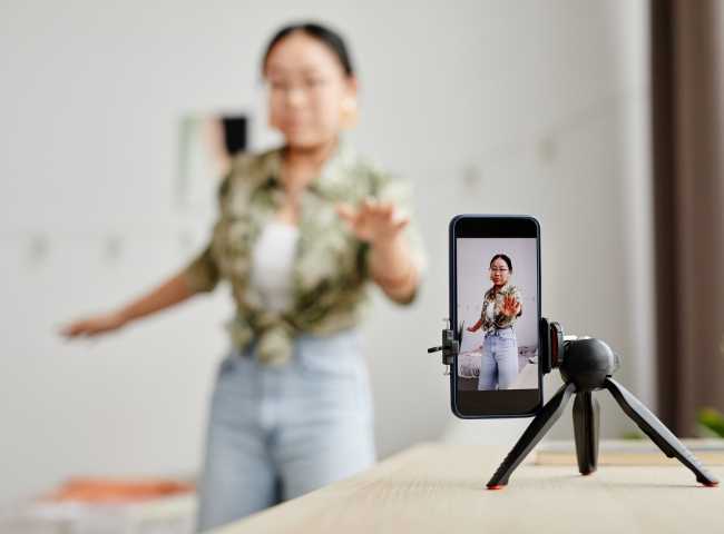 Woman recording a video on a smartphone using a tripod.